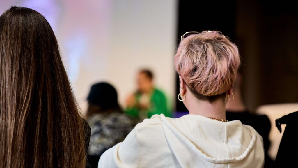 Rückansicht von zwei Personen mit langen und kurzen Haaren bei einem Talk mit unscharfem Hintergrund