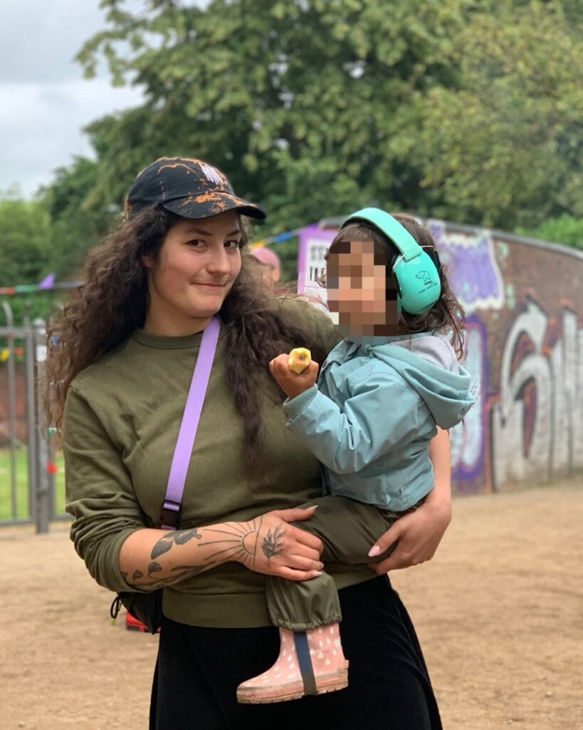 Person mit Baseballkappe hält Kind Gehörschutz auf dem Arm